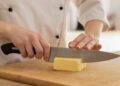 Cook cutting Butter with a chef knife on a board
