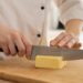 Cook cutting Butter with a chef knife on a board