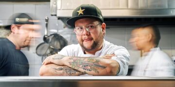 professional chef with tattoos on his arms on the pass in the kitchen