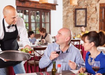 Professionele serveerder die een bord serveert aan een tafel in een restaurant, symbool voor respect voor serveerders in de horeca