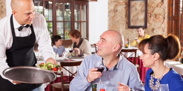 Serveur professionnel servant un plat à une table de restaurant, représentant le respect du serveur dans l'hospitalité