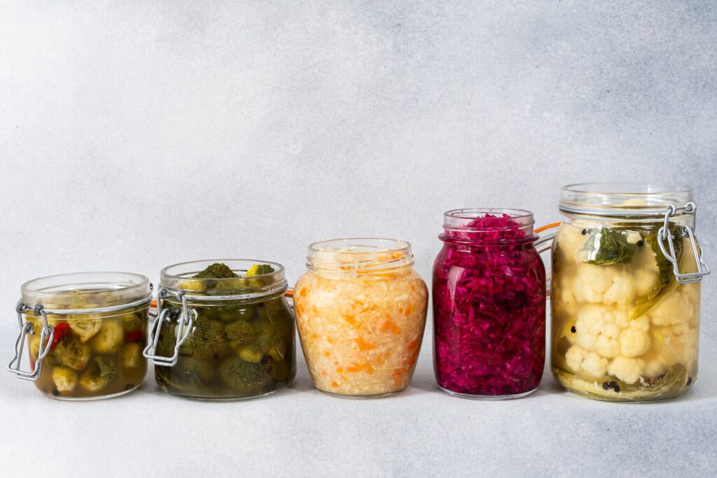 Traditionelles fermentiertes Gemüse in einem Keramiktopf mit frischem Kohl und Kräutern