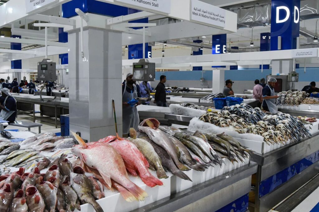 Rows of fresh fish on ice at a bustling seafood market stall with workers in the background.