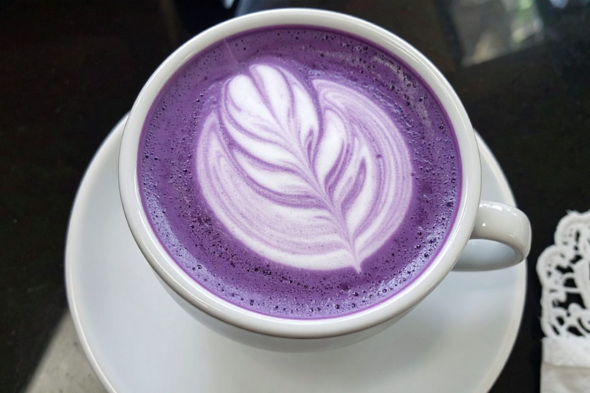 A smiling barista presenting a vivid ube purple yam latte with a rich violet swirl in a modern café setting