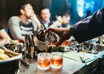 A bartender serves a premium spirit sample at the Food Festival, surrounded by enthusiastic visitors at an outdoor event.