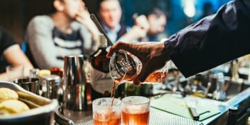 A bartender serves a premium spirit sample at the Food Festival, surrounded by enthusiastic visitors at an outdoor event.