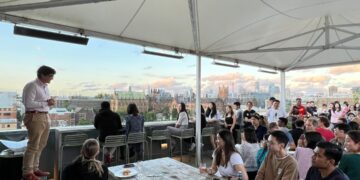 A chef carefully arranges light seasonal dishes on a rooftop dining terrace during a warm summer service