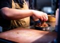 A chef carefully assembles a balanced grain bowl with layered grains, vegetables, and fresh herbs on a wooden counter