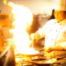 chef-charring-red-peppers-flame-unsplash - GUSTOwebzine Ein Koch hält mit einer Zange über einer offenen Flamme, während er Sommergemüse Paprika auf einem Gaskochfeld in einer professionellen Küche anröstet.