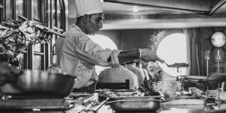 A professional chef stirs a deep pot of Neapolitan ragù over a low flame in a traditional kitchen