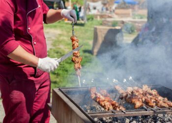 A professional chef arranges serving dishes at an outdoor catering station during a large off-site event.