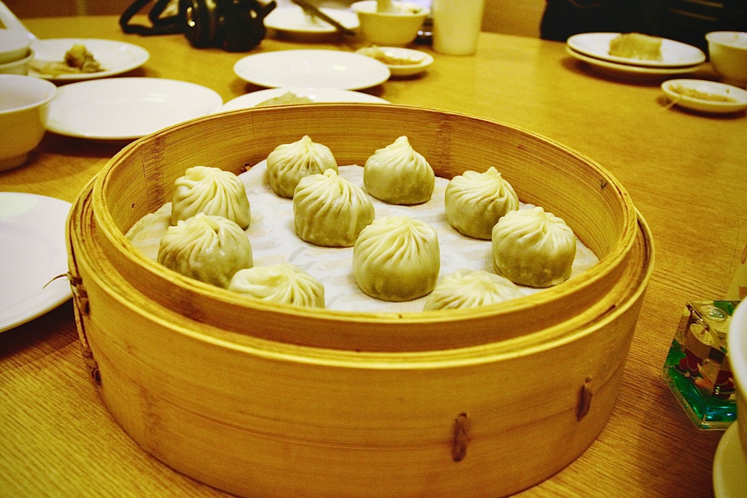 A chef lifting the lid of a bamboo steamer with dumplings, revealing the technique that gives this dish its delicate texture