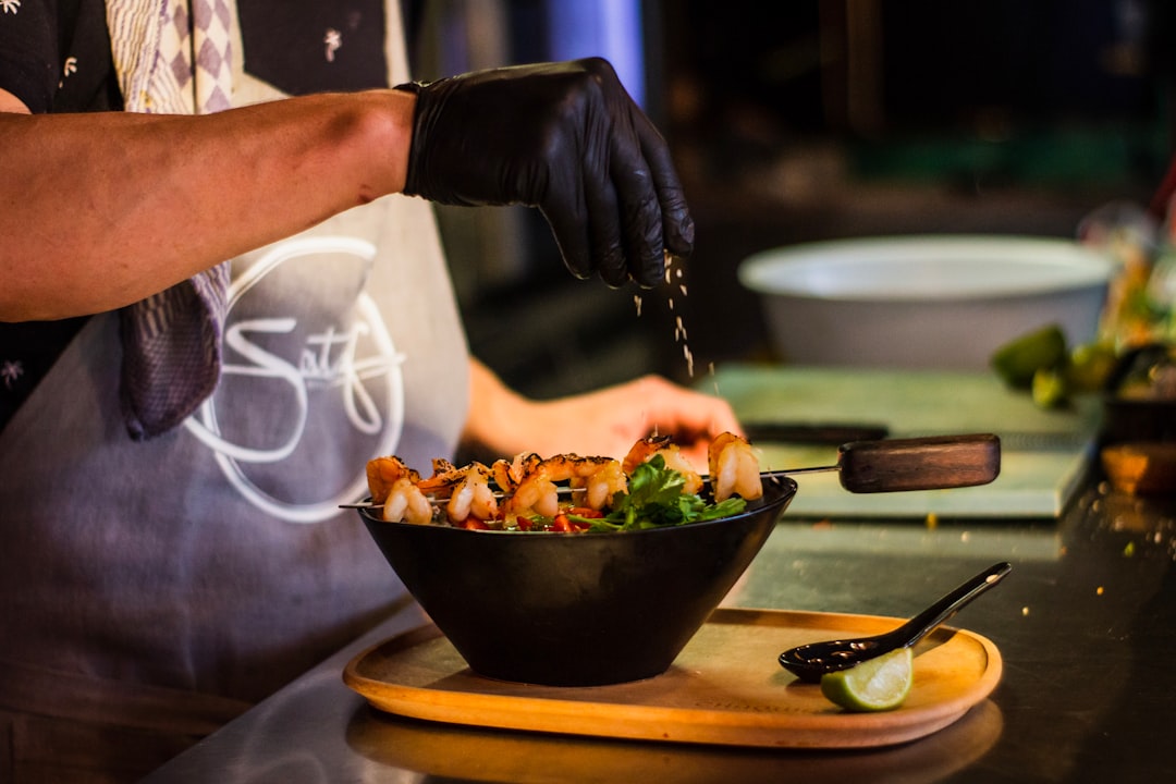 A cook drizzles a light tahini dressing over a finished grain bowl plated on a ceramic dish