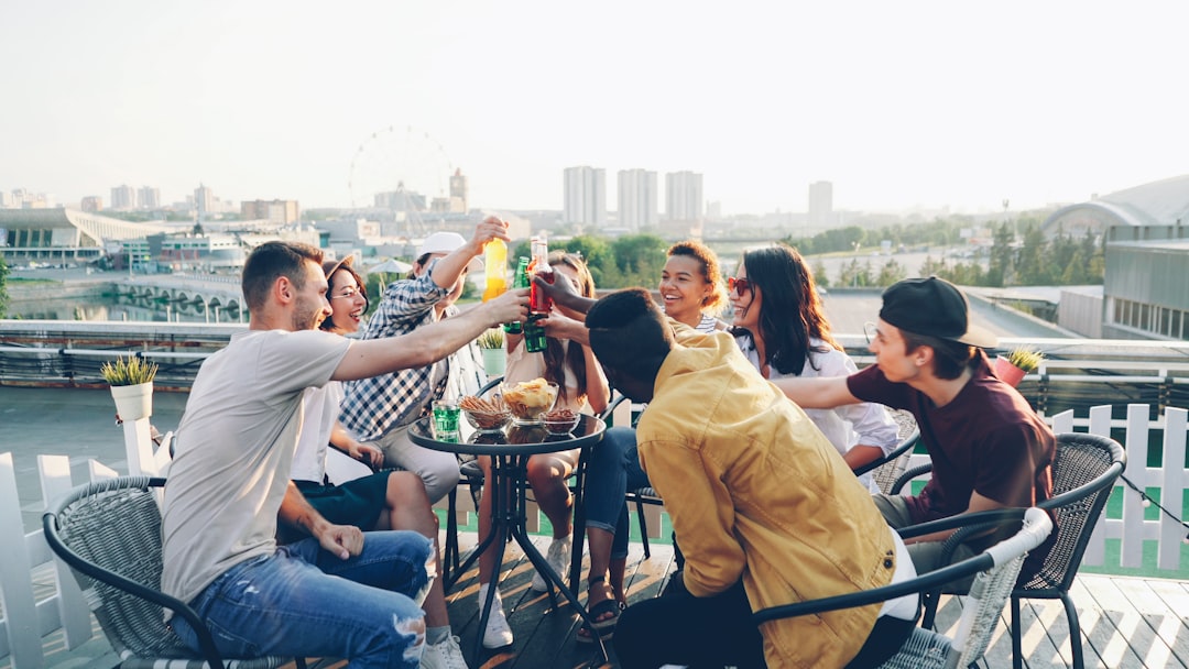 A group of friends clink their colorful spritz cocktails together at an outdoor terrace table on a warm sunny afternoon.