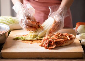 A woman prepares kimchi by hand, layering cabbage in a traditional crock, demonstrating the ancient craft behind this dish.