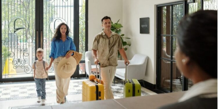 Private clubs Manhattan 7 most exclusive - GUSTOwebzine Family of three walks into a bright hotel lobby with yellow and green rolling suitcases as they enter through ornate glass doors.
