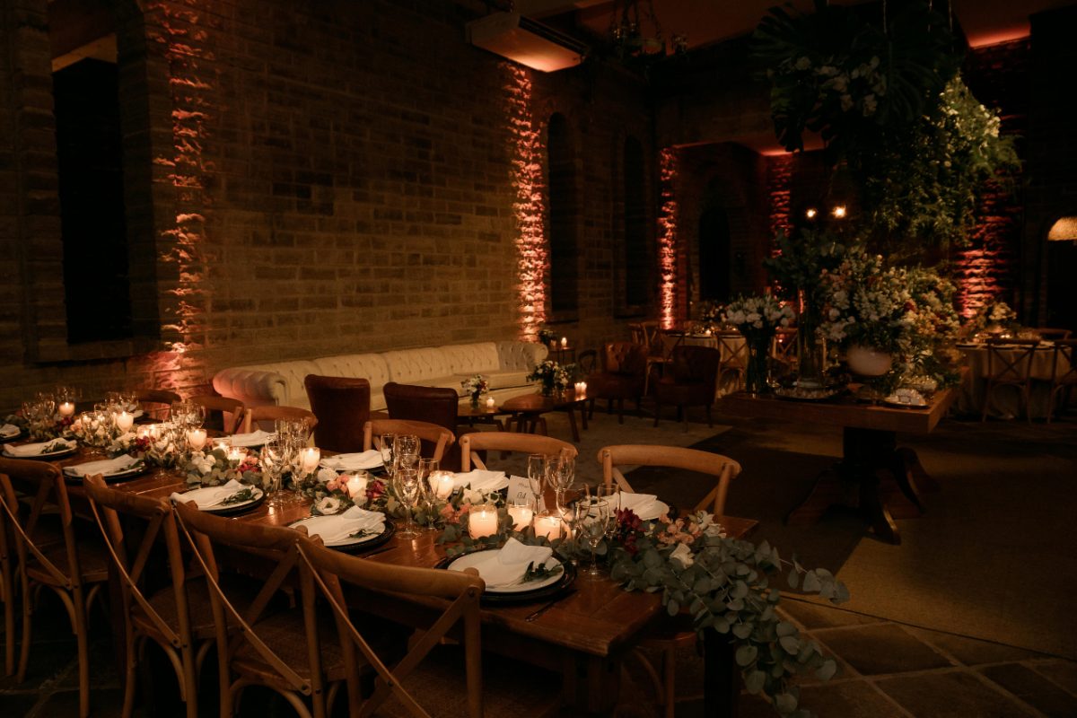 A waiter prepares candles and greenery on a restaurant terrace, creating ambiance for evening patio service.