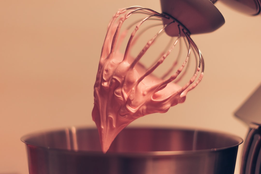 A person folding whipped cream into a mixing bowl while preparing homemade ice cream at home