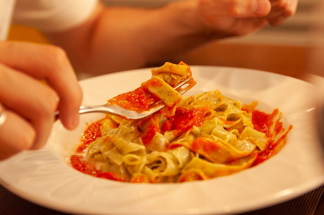 A person ladles slow-cooked Neapolitan ragù over a bowl of short ridged pasta at a wooden dining table