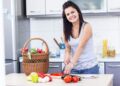 A woman carefully arranges containers of picnic recipes into a wicker basket on a kitchen, ready for a June outdoor outing.