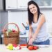 A woman carefully arranges containers of picnic recipes into a wicker basket on a kitchen, ready for a June outdoor outing.
