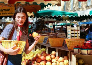 A woman carefully arranging ripe stone fruit at a summer farmers market, selecting the best peaches and plums for storage