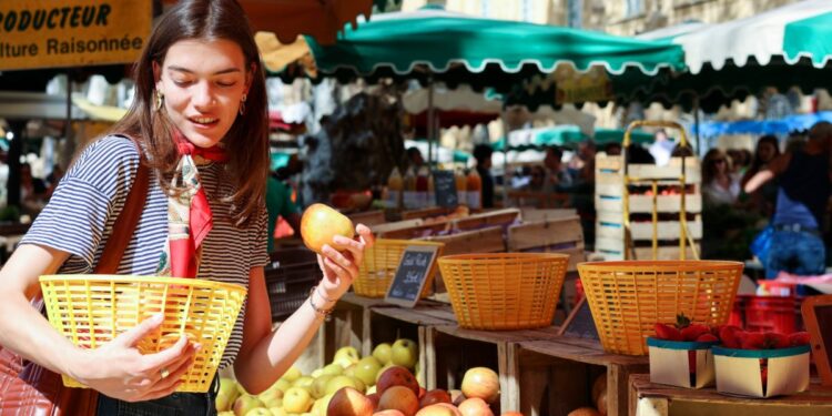 A woman carefully arranging ripe stone fruit at a summer farmers market, selecting the best peaches and plums for storage