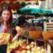 A woman carefully arranging ripe stone fruit at a summer farmers market, selecting the best peaches and plums for storage