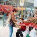 Woman in a mask buys sticky rice dumplings from a street vendor at an outdoor market stall with red baskets and stacked wraps on display.",