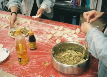 A woman folding handmade dumplings on a floured wooden surface, demonstrating the traditional craft behind this beloved dish