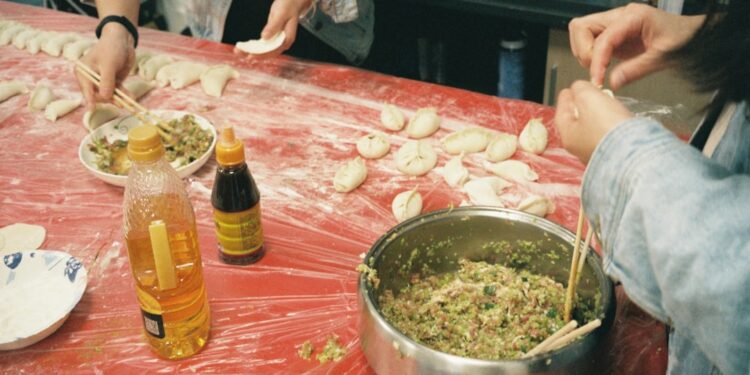 A woman folding handmade dumplings on a floured wooden surface, demonstrating the traditional craft behind this beloved dish