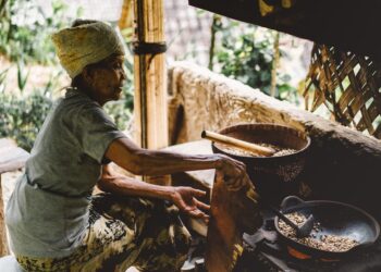 A woman carefully grinding aromatic spice blends from Africa using a traditional stone mortar and pestle in a home kitchen