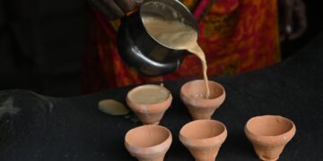 Filter coffee guide for home brewers in India - GUSTOwebzine Person pours beige batter from a metal pitcher into five small terracotta cups on a dark surface.