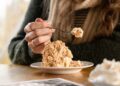 A woman scooping a bowl of homemade ice cream from a metal loaf pan in a bright kitchen