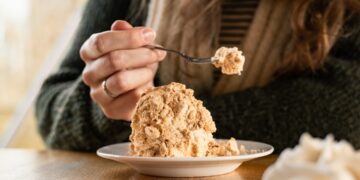 A woman scooping a bowl of homemade ice cream from a metal loaf pan in a bright kitchen