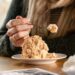 A woman scooping a bowl of homemade ice cream from a metal loaf pan in a bright kitchen