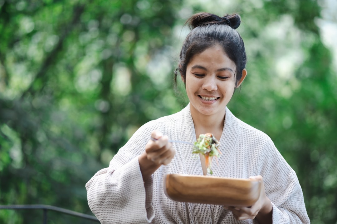 A woman tastes roasted miso-glazed vegetables at a kitchen counter, exploring the many culinary uses of miso paste.