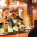 Bartender pouring whiskey from a bottle into a shaker for a customer at a bar by the counter.