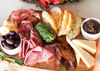 a colorful summer grazing board with global pantry staples including cured meats, cheese, and fresh fruit on a wooden surface