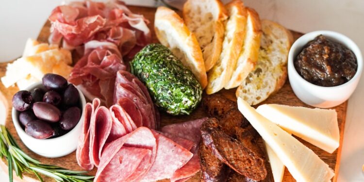a colorful summer grazing board with global pantry staples including cured meats, cheese, and fresh fruit on a wooden surface