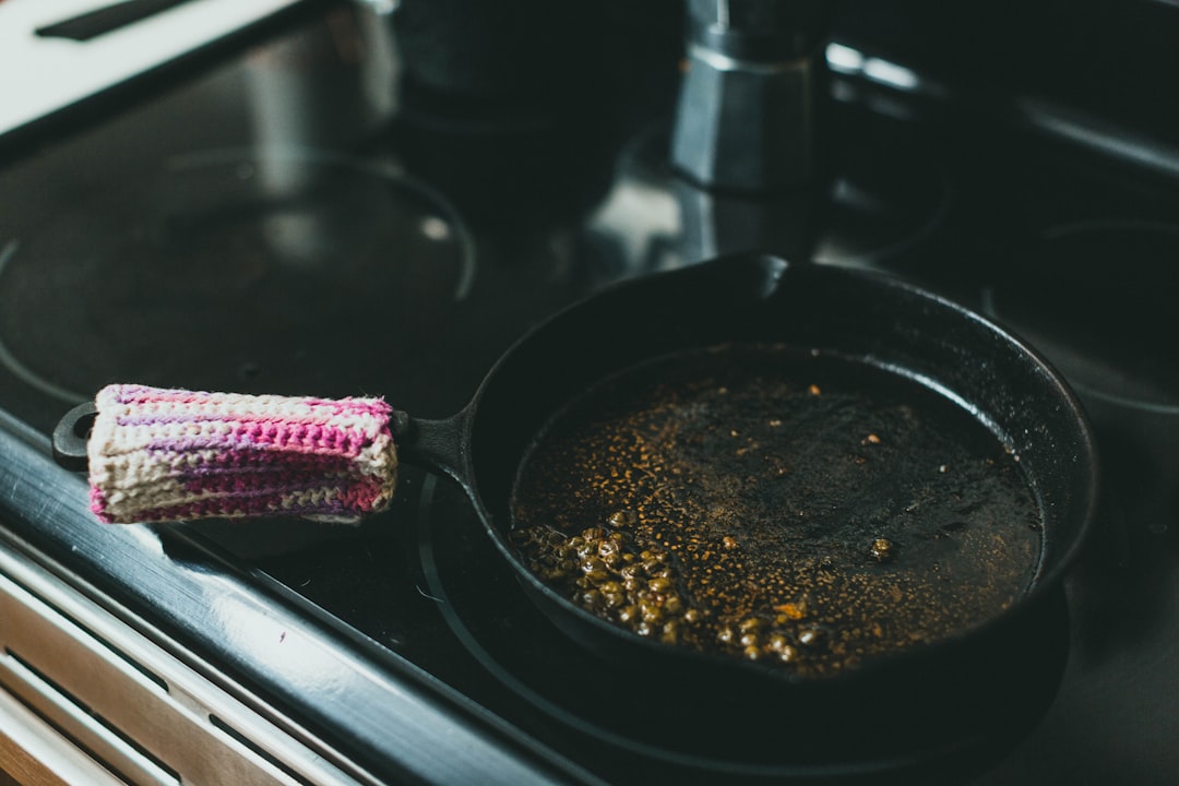 A chef carefully wipes and dries a cast iron pan on a stovetop to maintain its cast iron seasoning after cooking.
