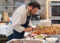 Un chef de hotel prepara cuidadosamente un plato de desayuno de hotel de origen local que presenta verduras estacionales y granos regionales