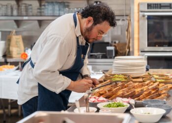 Ein Hotelkoch plattiert sorgfältig ein lokal bezogenes Hotelfrühstücksgericht mit saisonalem Gemüse und regionalen Körnern