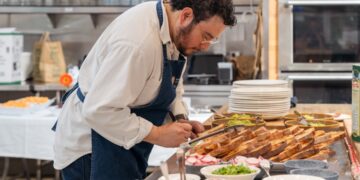 Un chef de hotel prepara cuidadosamente un plato de desayuno de hotel de origen local que presenta verduras estacionales y granos regionales