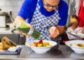 A chef carefully pouring chilled soups into a white bowl in a professional kitchen