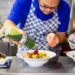 A chef carefully pouring chilled soups into a white bowl in a professional kitchen
