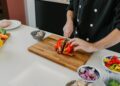 A chef demonstrating knife skills while slicing fresh summer tomatoes on a wooden cutting board