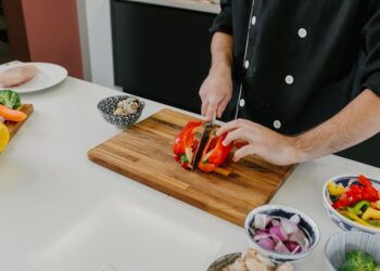 A chef demonstrating knife skills while slicing fresh summer tomatoes on a wooden cutting board