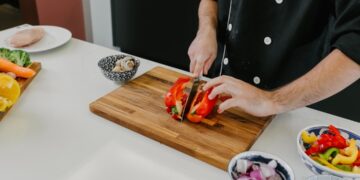 A chef demonstrating knife skills while slicing fresh summer tomatoes on a wooden cutting board