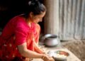 Harinas sin gluten para repostería india - GUSTOwebzine Mujer con un colorido sari rosa brillante corta verduras en una cocina exterior rústica, con boles de metal cerca.